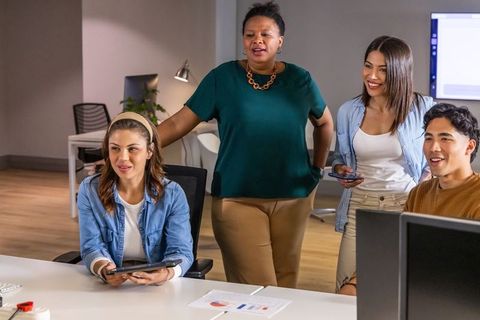 Diverse team collaborating around desk with tablet and printed charts in modern office
