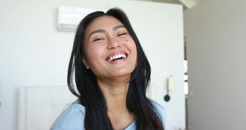 Smiling asian woman in minimalist bedroom embracing natural light and serene morning mood