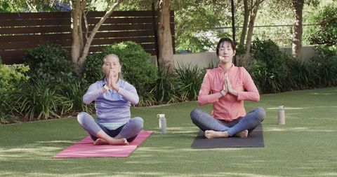 Asian Mother and Daughter Meditating on Yoga Mats in Garden