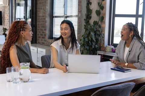 Diverse Female Coworkers Collaborate Around Laptop in Modern Office