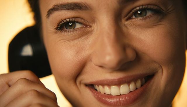 Smiling young woman holding retro handset near ear with warm backlight closeup