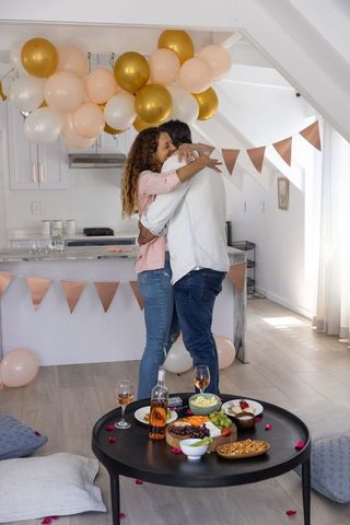 Mature couple embracing in decorated kitchen celebrating anniversary with rose and wine