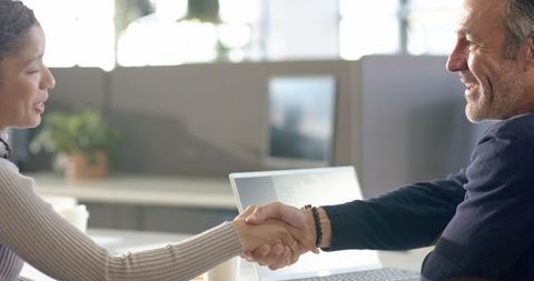 Shaking hands across modern office desk with laptop and coffee, collaboration and agreement