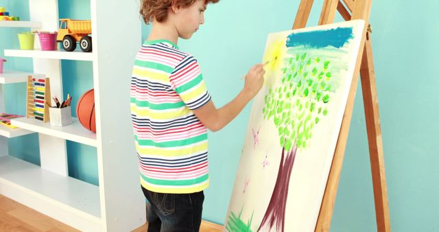 Focused caucasian preschool boy painting picture on easel in preschool room. Children, childhood, playing time and preschool activities, unaltered.