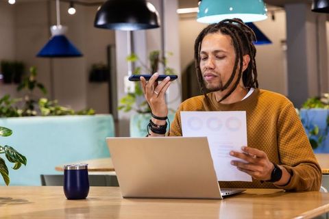 African American Man Using Smartphone Voice Assistant While Reviewing Charts in Office