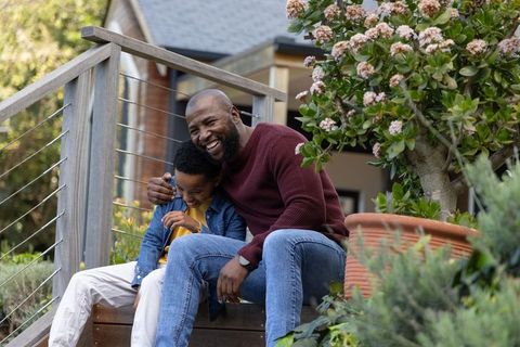 African american father laughing with son on porch steps beside flowering planter