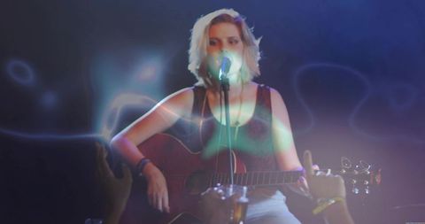 Indie singer performing with acoustic guitar under neon haze at intimate live venue