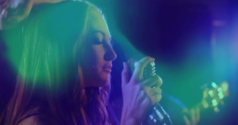 Female singer performing with retro microphone under colorful stage lights and hazy bokeh