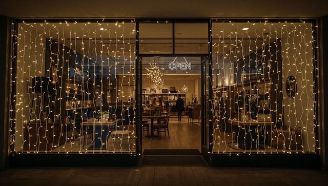 Cozy boutique storefront glowing with fairy lights and open neon sign at night
