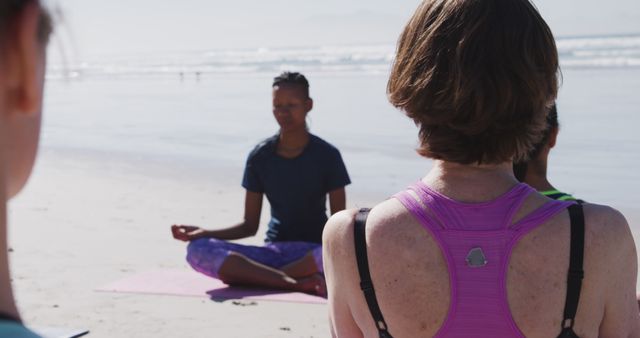 African American woman teaches yoga on the beach. She leads a serene outdoor class by the ocean, promoting wellness and tranquility.