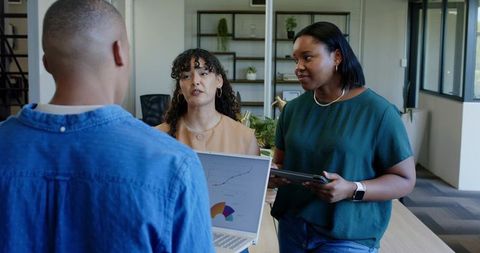 Diverse team collaborating around laptop and tablet presenting business charts in office