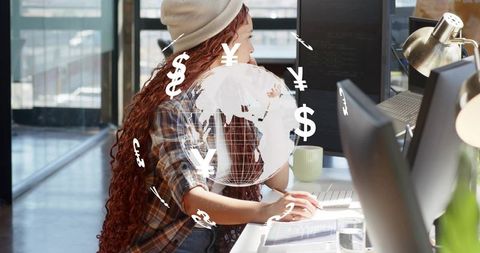 Young professional typing at modern office desk with globe and floating currency icons