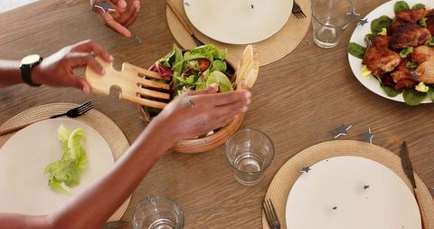 Tossing green salad with wooden tongs during casual family dinner on rustic wood table