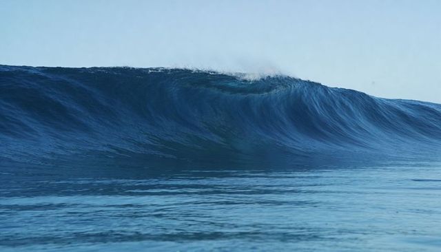 Deep-blue ocean swell building and breaking with crest spray over calm rippled sea
