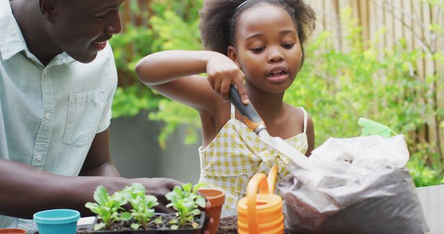 African American father and daughter planting potted plants together outdoors, bonding through gardening. The girl is using a small shovel to put soil into pots, while the garden tools and plants are spread out on the table. Ideal for family bonding, nature activities, and parenting content.