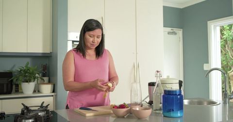 Asian woman peeling banana at modern kitchen island preparing healthy smoothie ingredients