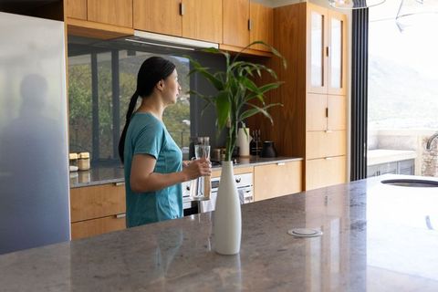 Mature african american woman holding water pitcher in modern kitchen overlooking patio