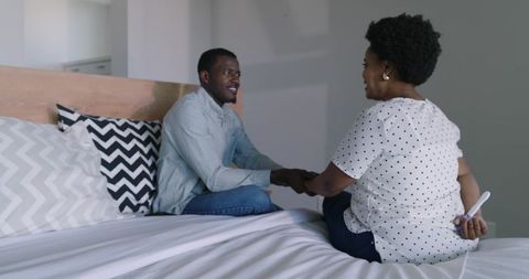 African american couple holding hands on bed while woman hiding pregnancy test