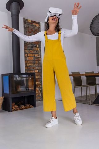 Woman exploring virtual reality wearing yellow overalls in modern home near wood-burning stove