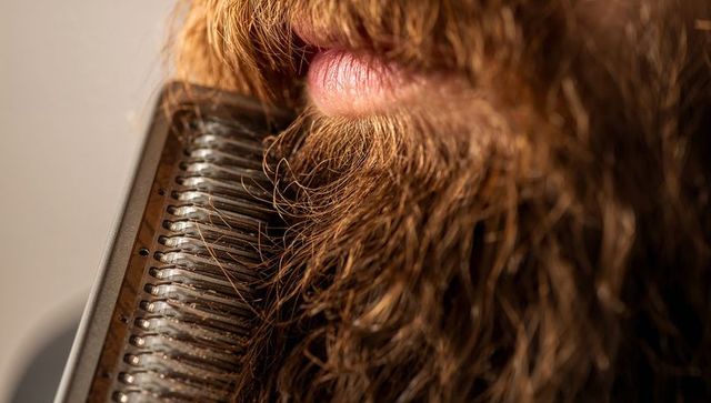 Trimming dense reddish-brown beard and mustache with metal trimmer head closeup