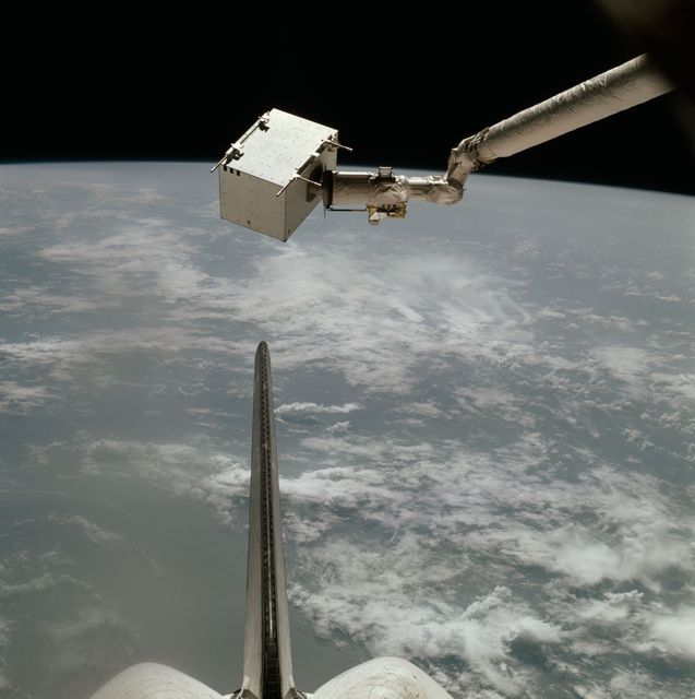 This image shows Space Shuttle Columbia's robotic arm holding an environment contaminant monitor over the North Atlantic Ocean during the STS-004 mission in 1982. The monitor checks for contaminants around the orbiter's cargo bay that could affect onboard experiments. Ideal for educational content on space missions, NASA history, robotic arms in space, Earth observation, and 1980s space technology.