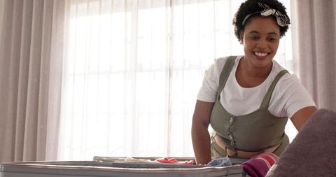 Smiling woman packing suitcase for vacation at home