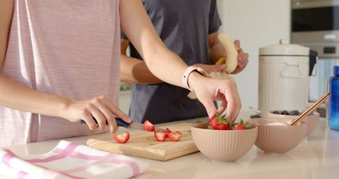 Couple preparing fresh fruit breakfast together in bright kitchen, slicing strawberries