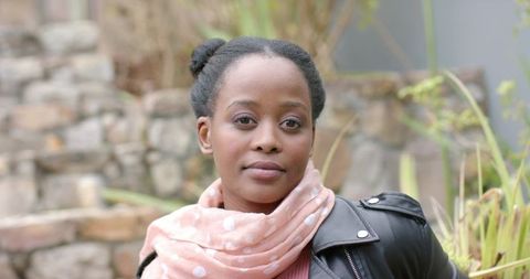 African american woman wearing pink polka-dot scarf and leather jacket posing in courtyard