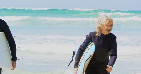 Senior Couple Running with Surfboards on Sunny Beach