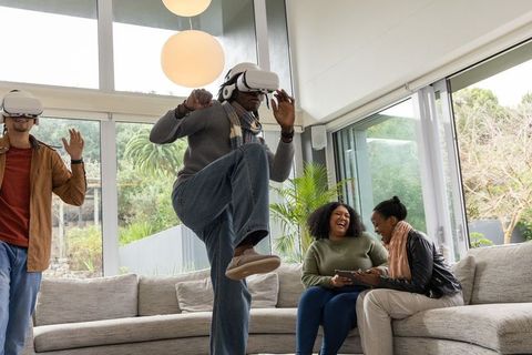 Diverse friends playing virtual reality at home laughing and interacting with tablet