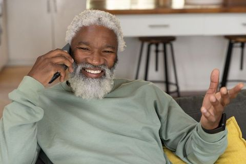 Senior african american man smiling and talking on smartphone while relaxing on sofa