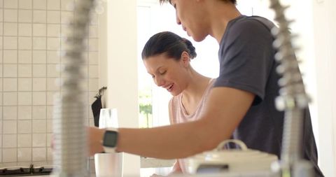 Young couple sharing sunny morning at modern kitchen counter, smiling, casual togetherness