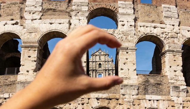 Hand framing ornate facade through arch at sunlit ancient amphitheater