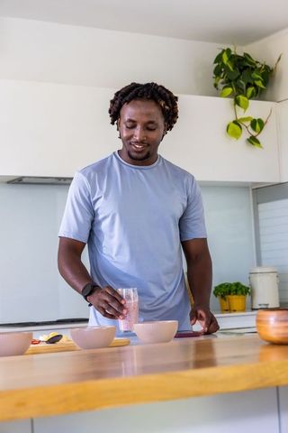 African american man preparing pink smoothie and arranging bowls at modern kitchen island