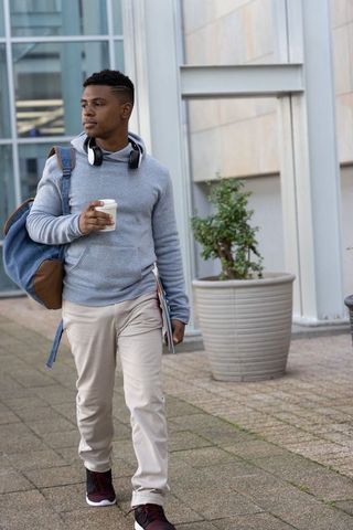 African american student walking with coffee and backpack on modern urban campus