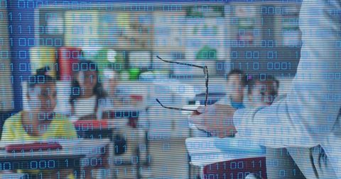 Mature teacher gesturing with glasses and binary overlay teaching digital coding classroom