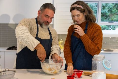 Middle-aged couple baking together in cozy kitchen mixing dough and savoring vanilla aroma