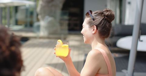 Diverse friends relaxing poolside on sunlit deck holding refreshing citrus drink