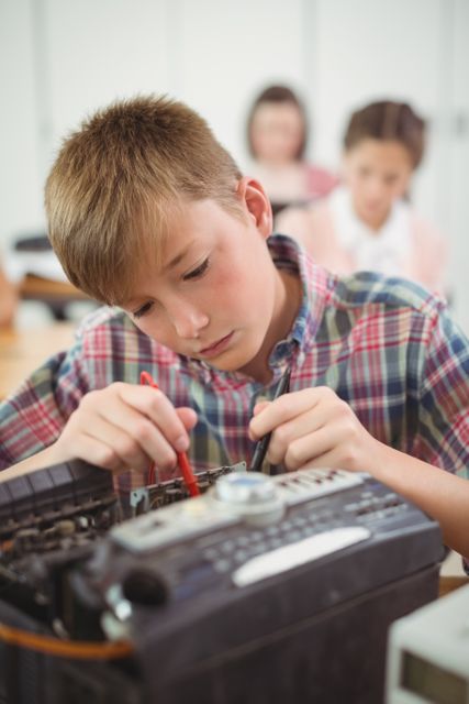 Young schoolboy in plaid shirt repairing a printer in a classroom, demonstrating hands-on learning and practical skills. Ideal for educational content, technology in schools, and promoting STEM activities.