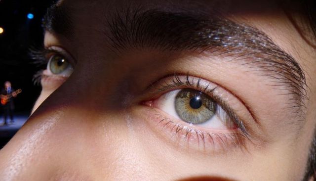Extreme closeup of male green-hazel eye with skin texture and concert stage bokeh