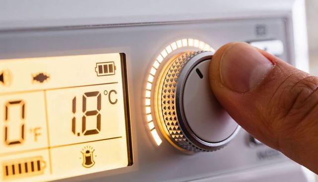Adult thumb turning backlit digital thermostat dial showing 1.8°c home temperature