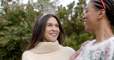 Friends sharing joyful moment in garden wearing cozy sweaters and festive headband