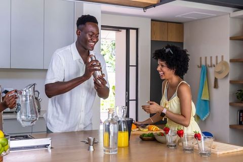 African american couple making cocktails and laughing in modern bright kitchen