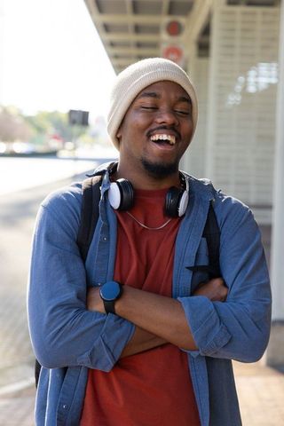African american commuter laughing on platform wearing beanie headphones and backpack