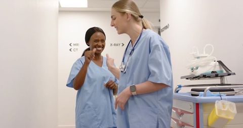 Diverse female nurses walking and talking in hospital corridor near radiology signage