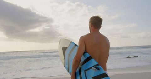 Surfer standing at tranquil beach holding surfboard at sunset
