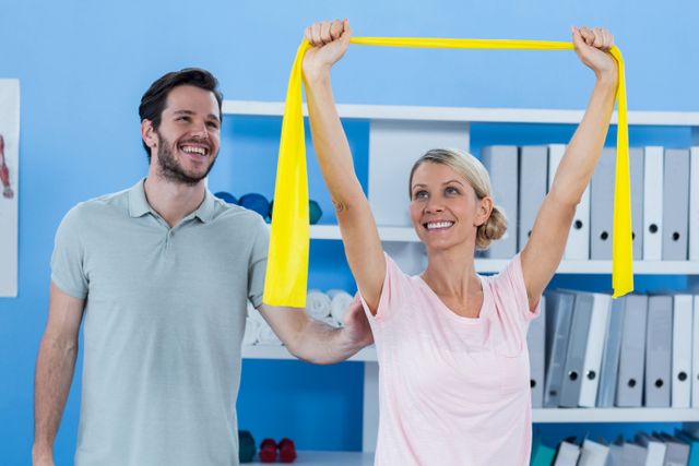 Physiotherapist assisting female patient with resistance band exercise in a clinic. Ideal for use in healthcare, physical therapy, rehabilitation, and wellness contexts. Can be used in articles, brochures, and websites related to medical treatment, patient care, and fitness programs.