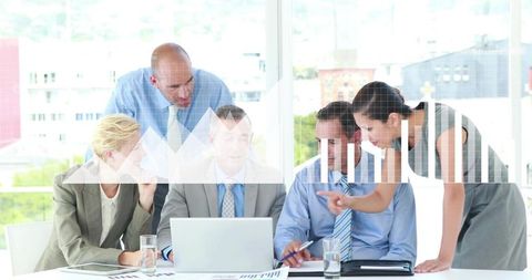 Collaborative team analyzing financial charts on laptop as woman points in boardroom