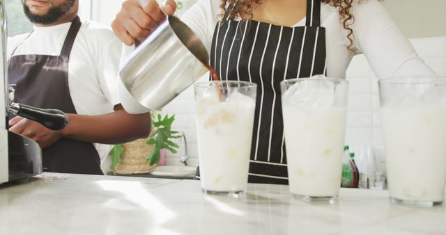 Baristas pouring coffee into iced glasses in modern cafe. Perfect for articles about coffee shop culture, teamwork in cafes, barista training, or promoting coffee-related products and services.
