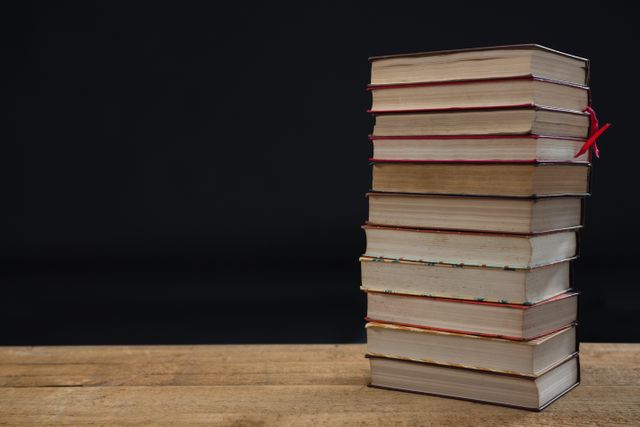 Stack of hardcover books on wooden table with black background. Ideal for educational content, library promotions, reading campaigns, and academic materials. Suitable for illustrating concepts of knowledge, learning, and literature.